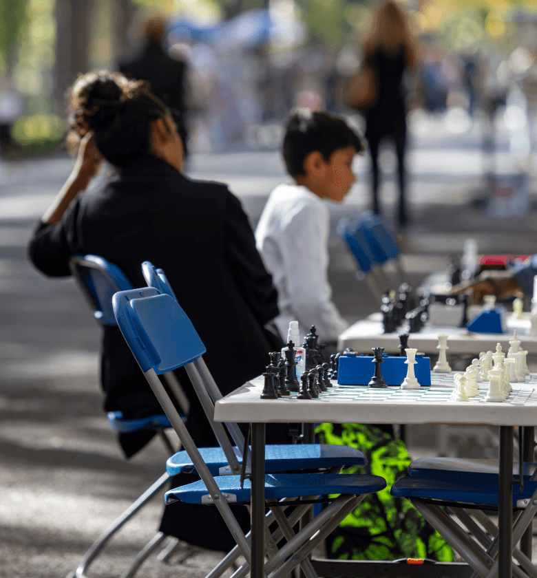 People gathered around chess tables at a park enjoying a chess match near The Henry UWS condominiums for sale.